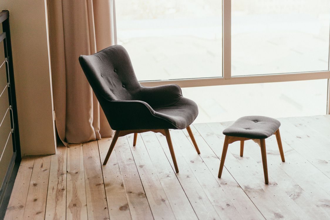 An empty armchair and footstool beside a window in a bright interior
