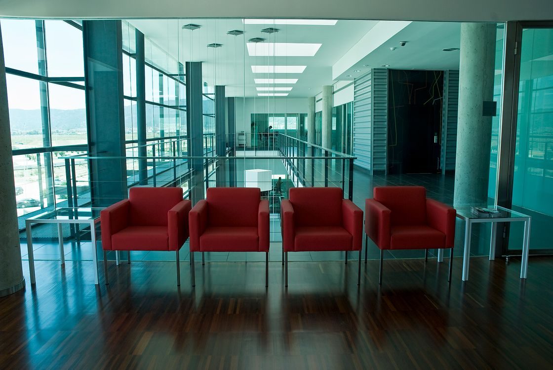 Empty modern office lobby with a row of red armchairs and floor-to-ceiling glass walls