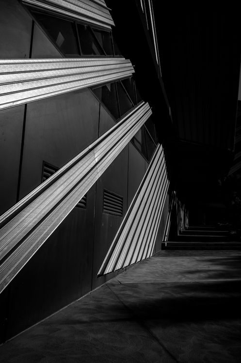 A dark angular building facade lit by diagonal beams of light