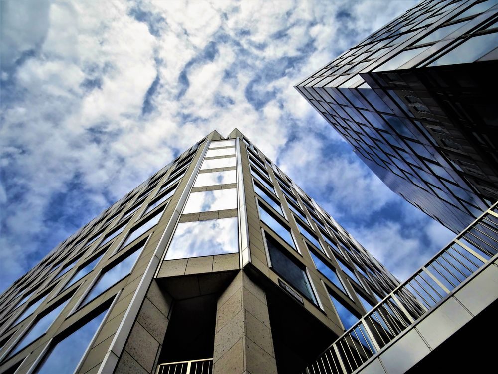 Low-angle view of modern glass office towers against a cloudy blue sky