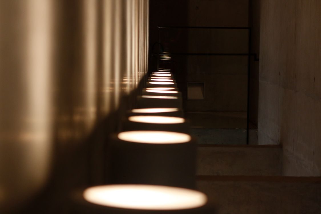 A dim corridor of repeating pillars with recessed downlights receding into the distance