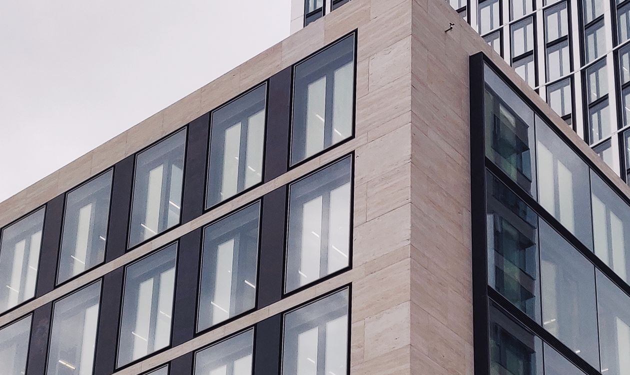 A modern office building with a grid of dark-framed windows and a taller glass tower behind it